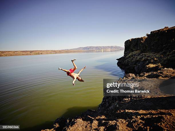 young man doing a backflip off cliff into river - diving risk stock-fotos und bilder