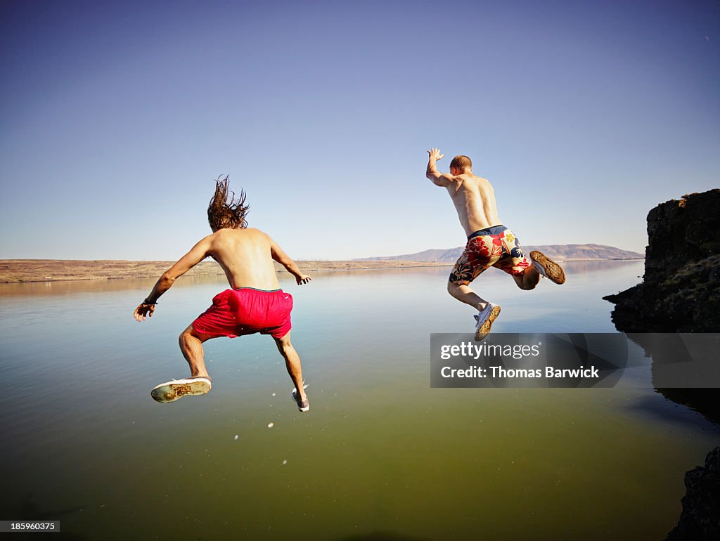 Two male friends jumping into river together
