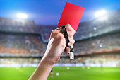 Referee holding up a red card and whistle inside a stadium