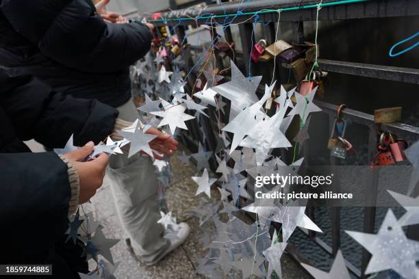 December 2023, Hamburg: Schoolgirls attach homemade stars made from the aluminum lids of yogurt and pudding cups to the Michaelis Bridge in the city...