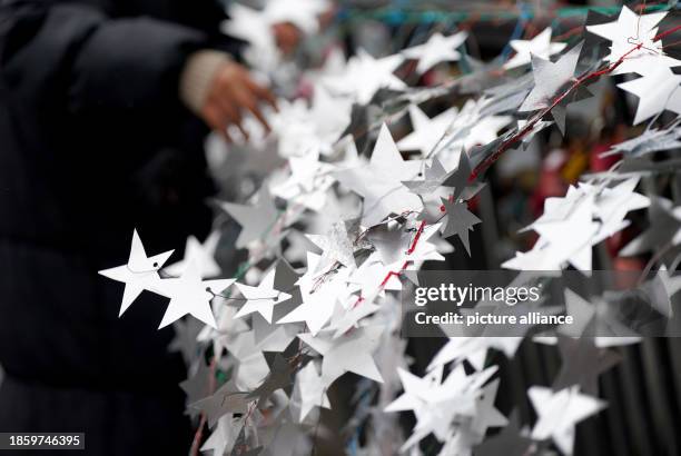 December 2023, Hamburg: Schoolgirls attach homemade stars made from the aluminum lids of yogurt and pudding cups to the Michaelis Bridge in the city...