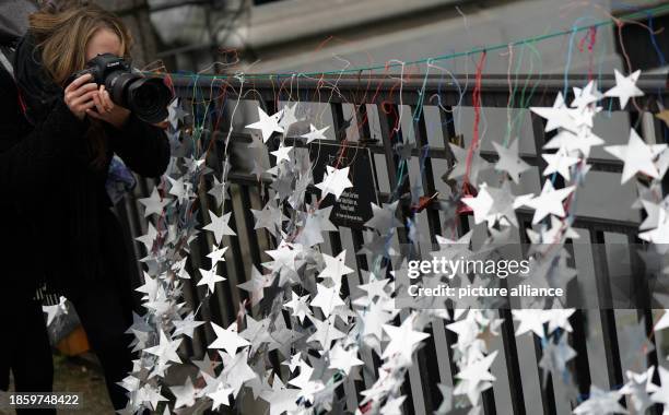 December 2023, Hamburg: A woman photographs the homemade stars made from aluminum lids from yogurt and pudding cups on the Michaelis Bridge in the...
