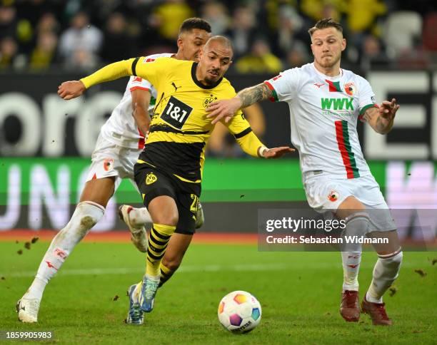 Donyell Malen of Borussia Dortmund is challenged by Felix Uduokhai and Jeffrey Gouweleeuw of FC Augsburg during the Bundesliga match between FC...
