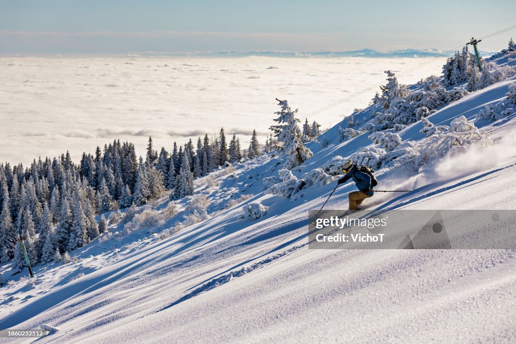 Back country skier riding on high mountain slope above the clouds