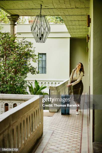 wide shot smiling woman walking though courtyard of hotel with luggage - lampshade skirt stock pictures, royalty-free photos & images