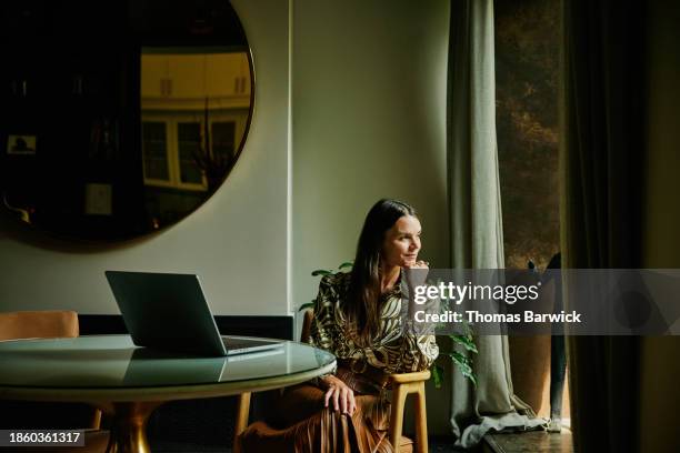wide shot businesswoman working on laptop looking out window of hotel - luxury women stock pictures, royalty-free photos & images