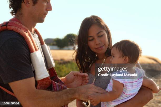 father reaches for baby girl held by mother - redondo beach kalifornien stock-fotos und bilder