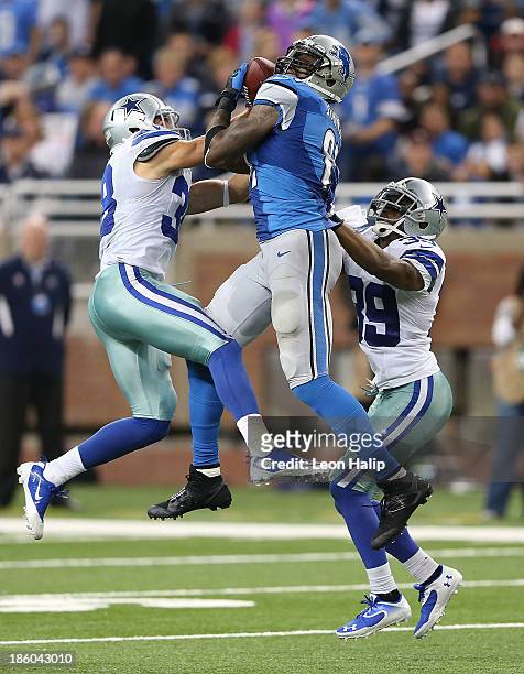 Calvin Johnson of the Detroit Lions leaps between Jeff Heath and Brandon Carr of the Dallas Cowboys and makes a 54 yard catch during the fourth...