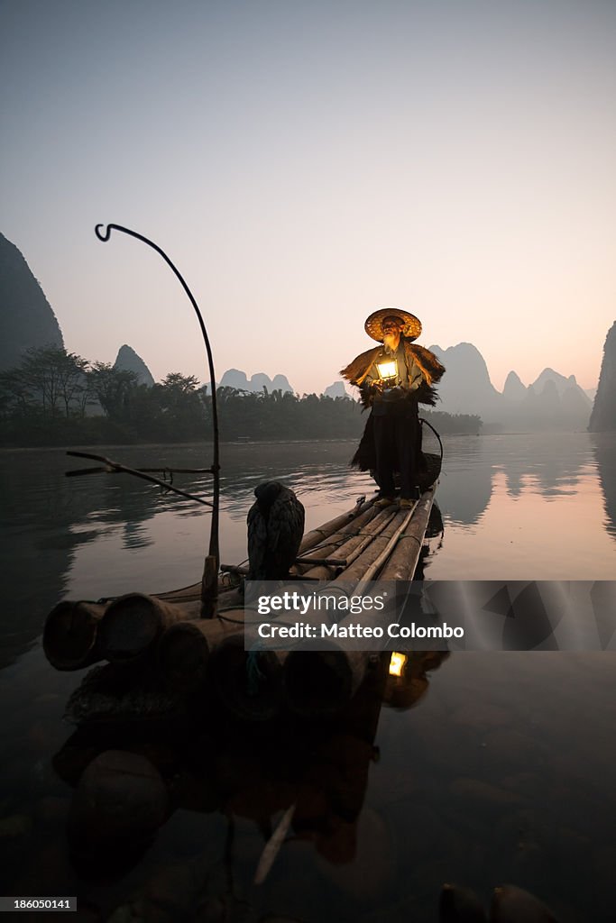 Fisherman with cormorants holding lantern, at dawn