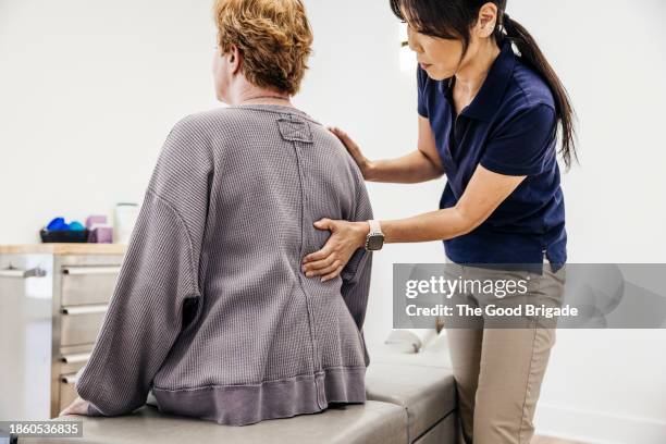 female osteopath examining senior woman's back at clinic - backache stock pictures, royalty-free photos & images