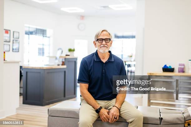 portrait of cheerful male chiropractor sitting at medical clinic - navy blue polo shirt stock pictures, royalty-free photos & images