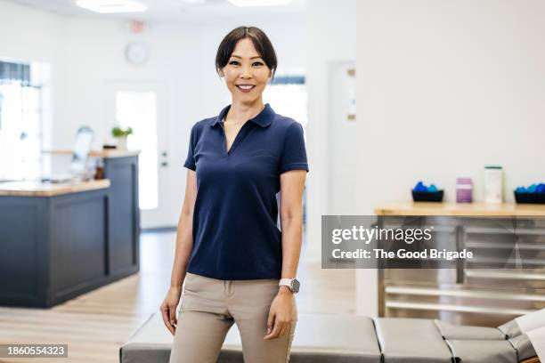 portrait of smiling mature female osteopath standing at clinic - fisioterapista foto e immagini stock