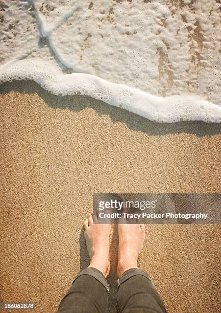 a pair of bare feet on sand await the wave - mens bare feet fotografías e imágenes de stock