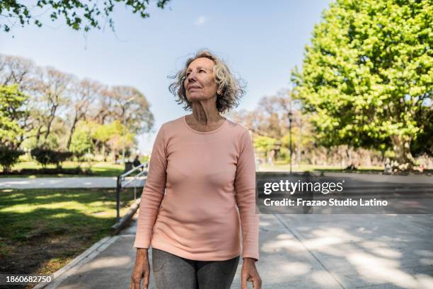 mujer mayor contemplando y caminando en el parque público - mirar alrededor fotografías e imágenes de stock
