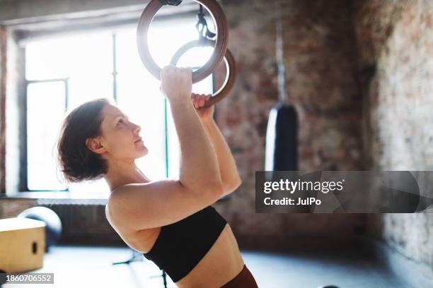 mid adult woman doing exercises on gymnastic rings in gym - gymnastic rings stock pictures, royalty-free photos & images