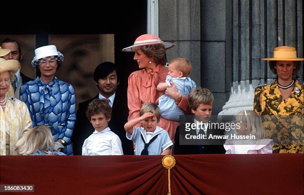 Diana, Princess of Wales, wearing a peach dress with a pussy bow tie designed by Jan Van Velden and a hat by Frederick Fox, carries baby Prince Harry...