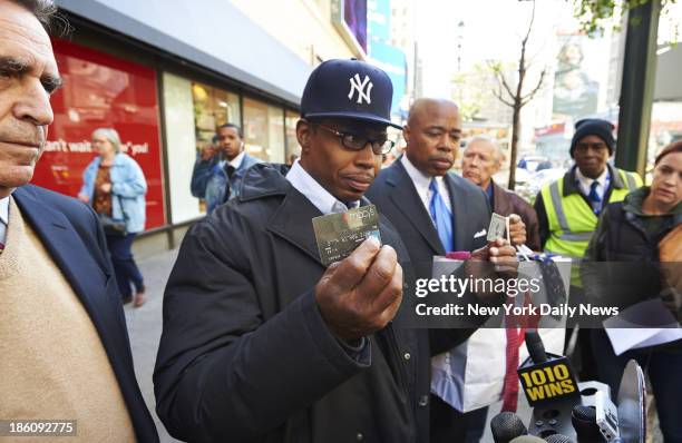 Art Palmer, of Brooklyn, center, holds up his Macy's and American Express cards at a press conference with New York State Senator Eric Adams, right,...