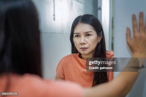 woman looking into mirror with mixed emotion - midlife crisis stock pictures, royalty-free photos & images