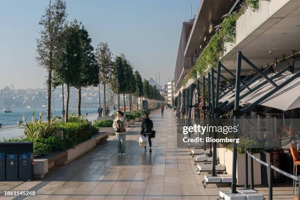 Pedestrians walk along the banks of the Bosphorus strait, alongside restaurant terraces at Galataport in the Karakoy district of Istanbul, Turkey, on...