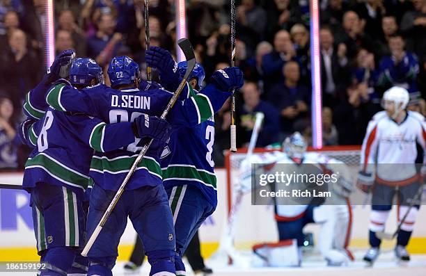 Daniel Sedin of the Vancouver Canucks is congratulated by Henrik Sedin and Chris Tanev after scoring a goal on goalie Michal Neuvirth of the...