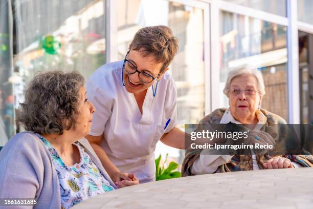 nurse visiting seniors sitting in the garden of a geriatric - geriatria fotografías e imágenes de stock