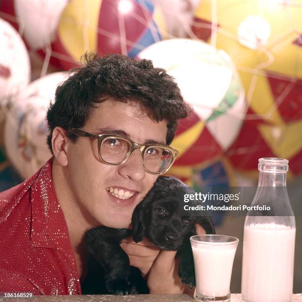 Italian singer Peppino di Capri hugging a puppy and smiling. 1964.