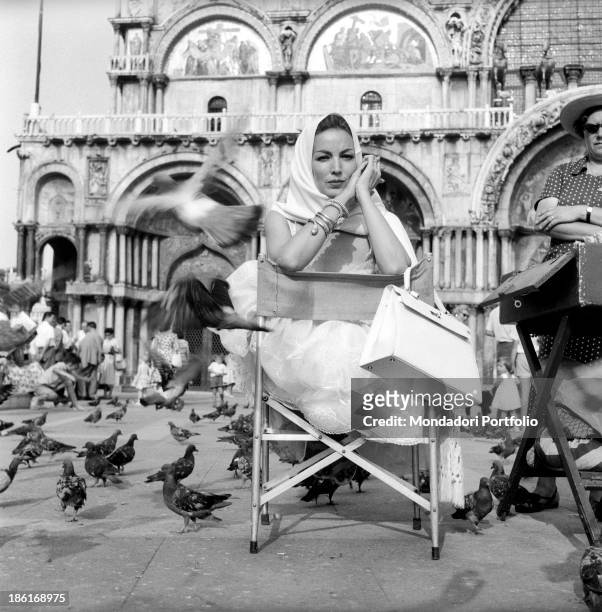 Mexican actress Maria Félix sitting on a folding chair in Piazza San Marco surrounded by the pigeons. She's taking part in the Venice Film Festival....