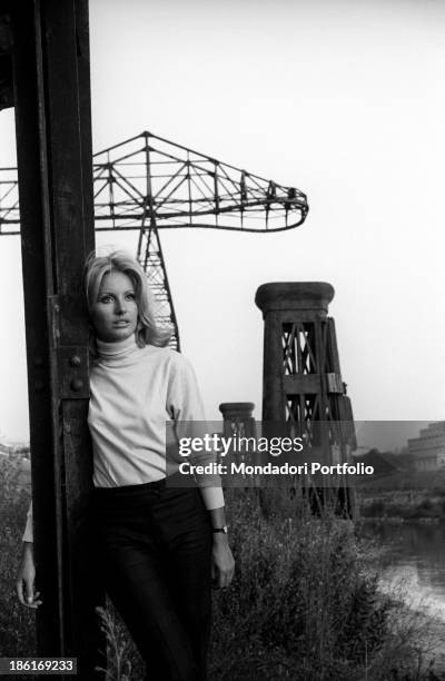 Italian TV presenter and actress Gabriella Farinon posing leaning against a pylon. Italy, 1968.