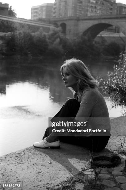 Italian TV presenter and actress Gabriella Farinon sitting on a river bank. Italy, 1968.