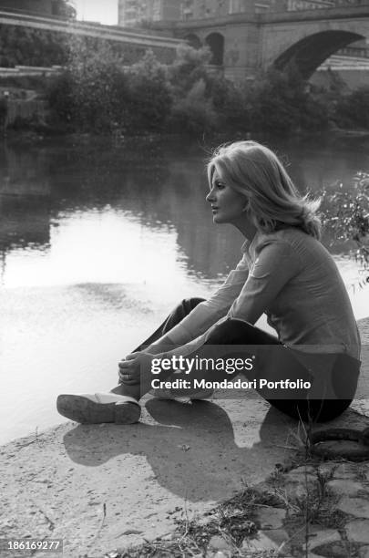 Italian TV presenter and actress Gabriella Farinon sitting on a river bank. Italy, 1968.