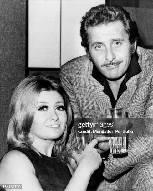 Italian singer-songwriter and actor Domenico Modugno smiling with a glass in his hand beside Italian actress Paola Quattrini. October 1969.