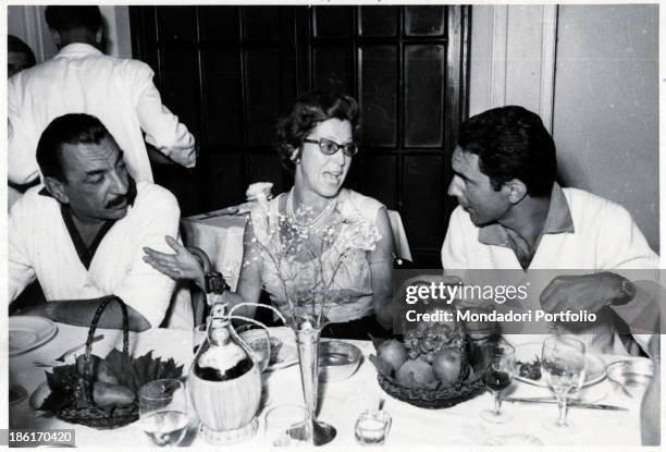 Italian publisher Alberto Mondadori sitting at a table with Italian journalist and writer Italo Calvino and Albertina Antonelli, wife of Italian...