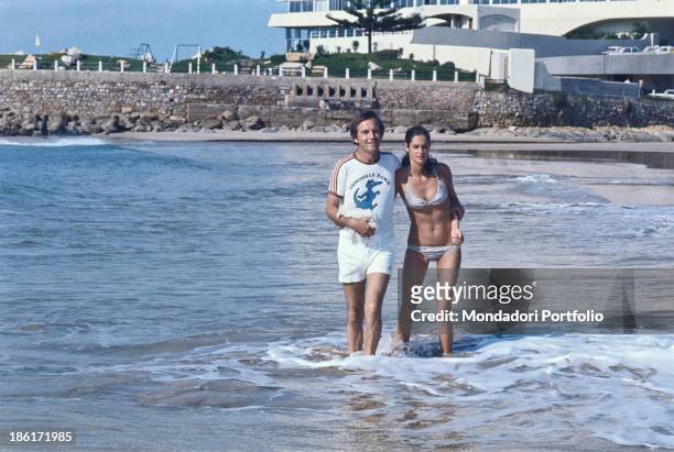 South African surgeon Christiaan Barnard walking hugging his wife Barbara Zoellner by the sea. Plettenberg Bay, 1977.