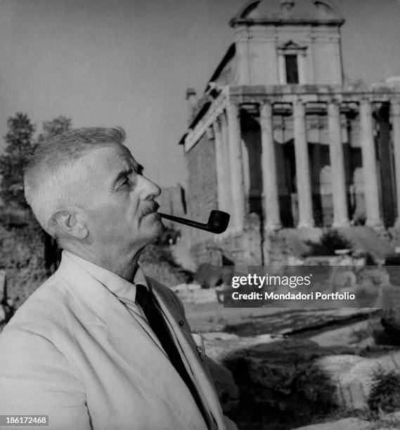 American writer William Faulkner smoking the pipe beside an archaeological site. Rome, September 1955.