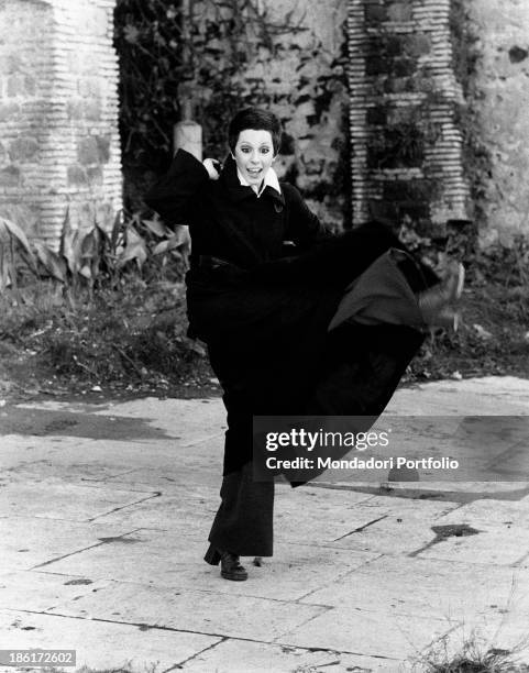 The Italian actress and singer Daniela Goggi, wearing a dark coat, dark trousers and heeled boots, is improvising a dance movement; the artist has...