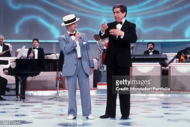 Italian television and radio presenter and writer Corrado gesticulating next to a competitor on the stage of TV show La Corrida. Italy, 1986.