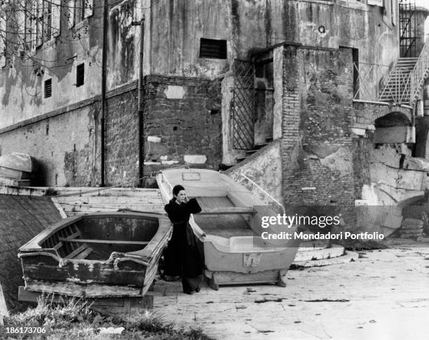 The Italian actress and singer Daniela Goggi wearing a dark coat between two rowboats by a small dock along the Tiber river; she is the younger...