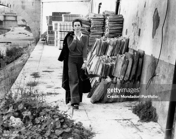 The Italian actress and singer Daniela Goggi is walking towards the photographer keeping her coat hanging on her back; behind her some piles of...