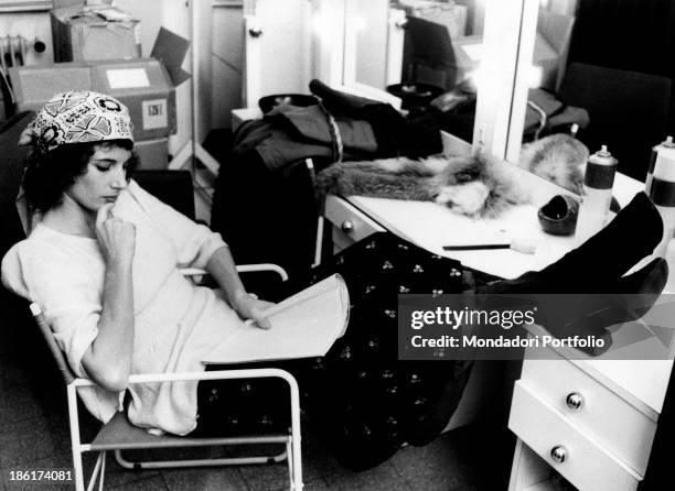 The Italian film, theatre and television actress Paola Pitagora is studying a script while seated on a chair in her dressing room, with her legs...