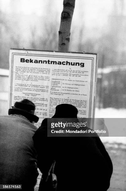 Two West Berliners reading a notice of the rules for obtaining a Christmas pass to the eastern zone, West Berlin, December 1963.