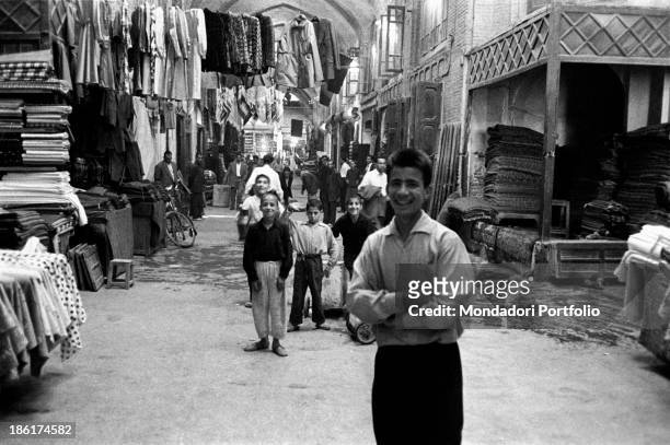 Some children and young boys standing in an indoor market selling clothes. Tehran, September 1957.