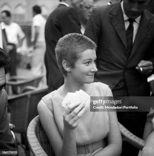 Italian actress Carla Gravina smiling holding a sandwich at the International Film Festival. She shaved her hair for the film Five Branded Women....