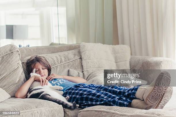 boy lying on a couch in his pj's cuddling his cat - sapato cor de creme - fotografias e filmes do acervo