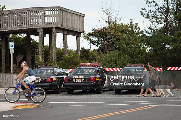 Bicyclist and pedestrians with a dog pass parked police cruisers on Long Beach Island in Long Beach Township, New Jersey, U.S., on Thursday, Sept....