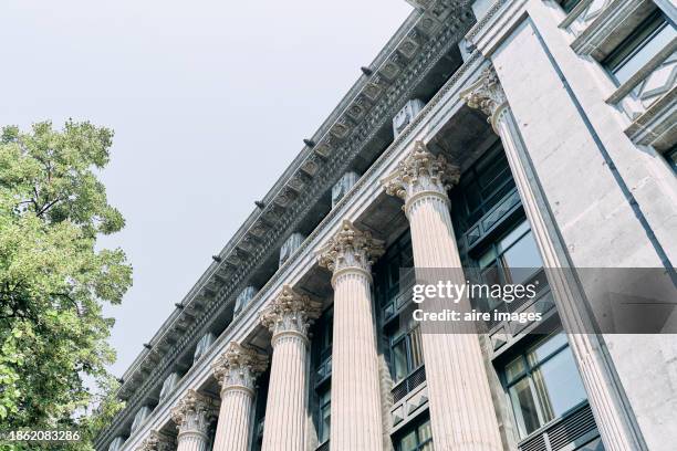 low angle view of the exterior of a building with windows and columns in bilbao with trees around, sky in background - treasury stock pictures, royalty-free photos & images