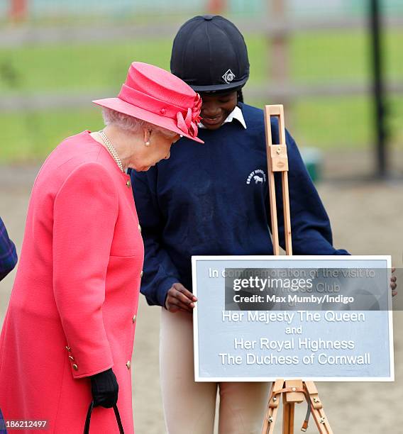 Queen Elizabeth II unveils a plaque as she, accompanied by Camilla, Duchess of Cornwall, visits the Ebony Horse Club and Community Riding Centre on...
