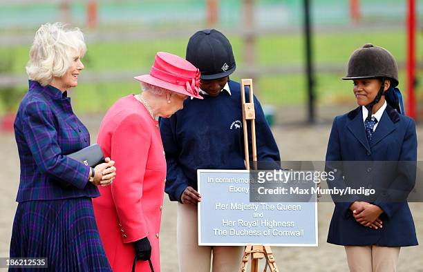 Camilla, Duchess of Cornwall looks on as Queen Elizabeth II unveils a plaque during a visit to the Ebony Horse Club and Community Riding Centre on...