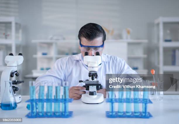laboratory technician looking through microscope while examining genomic sample during research in laboratory - stem cell stock pictures, royalty-free photos & images
