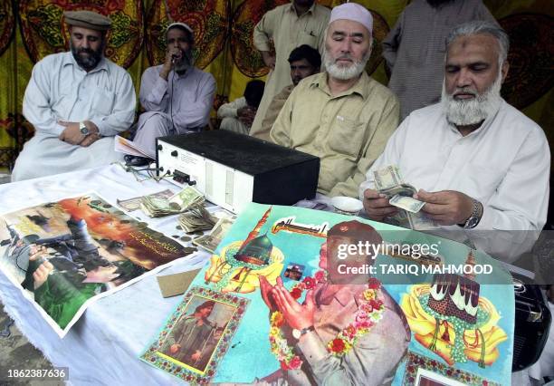 Worker of a Pakistan's six-party religious alliance of Muttahida Majlis-e-Amal counts money beside a poster of Iraqi President Saddam Hussein at a...