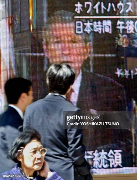 Pedestrians watch a large TV screen in Tokyo, 20 March 2003, showing US President George W. Bush delivering speech to launch war against Iraq. Japan...